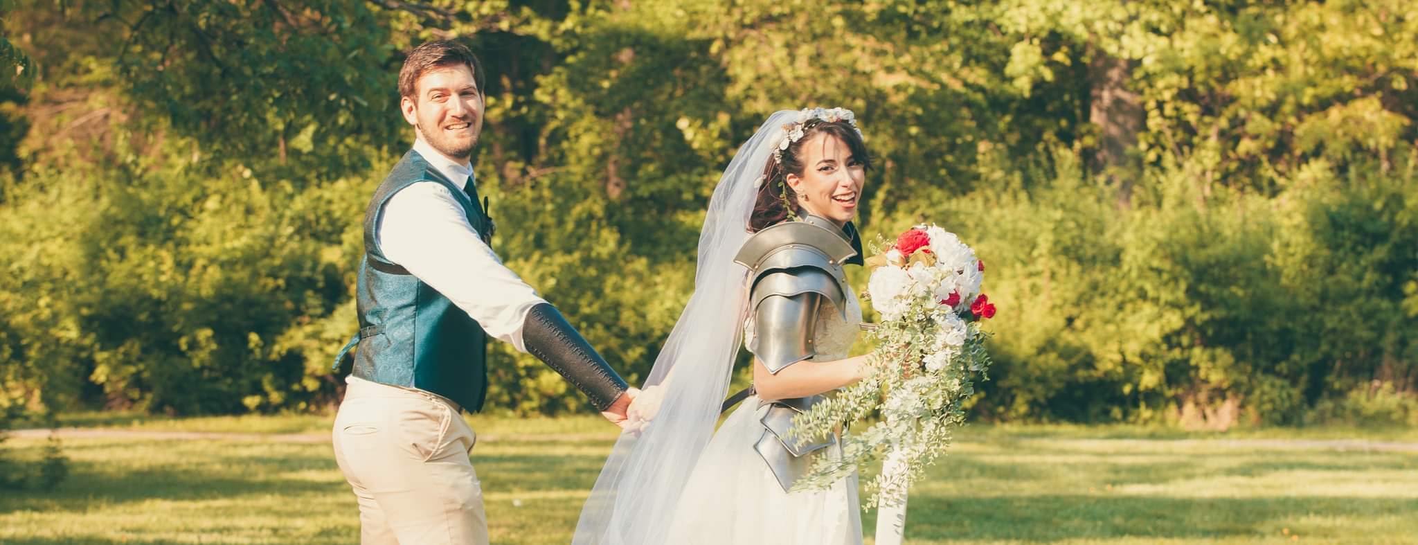 A couple holding hands outdoors with trees and grass in the background, the woman holding a bouquet of flowers.