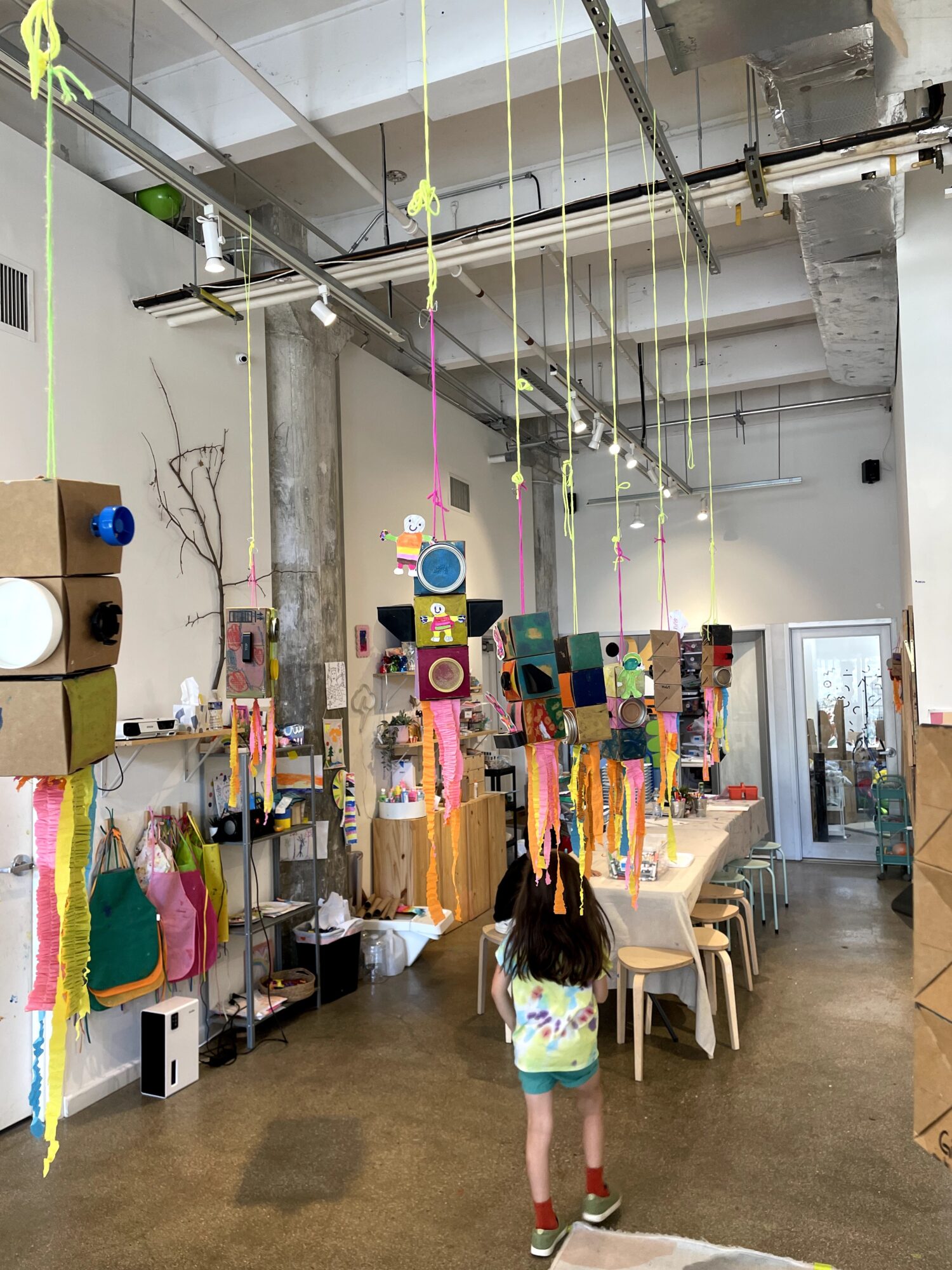 Child standing in a colorful craft store with hanging decorations and shelves filled with art supplies.