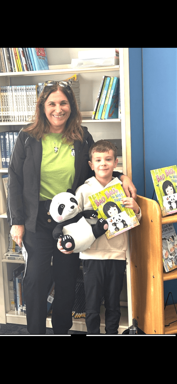 Woman and boy holding panda plush toys in a bookstore, bookshelves in background, smiling, bright lighting.