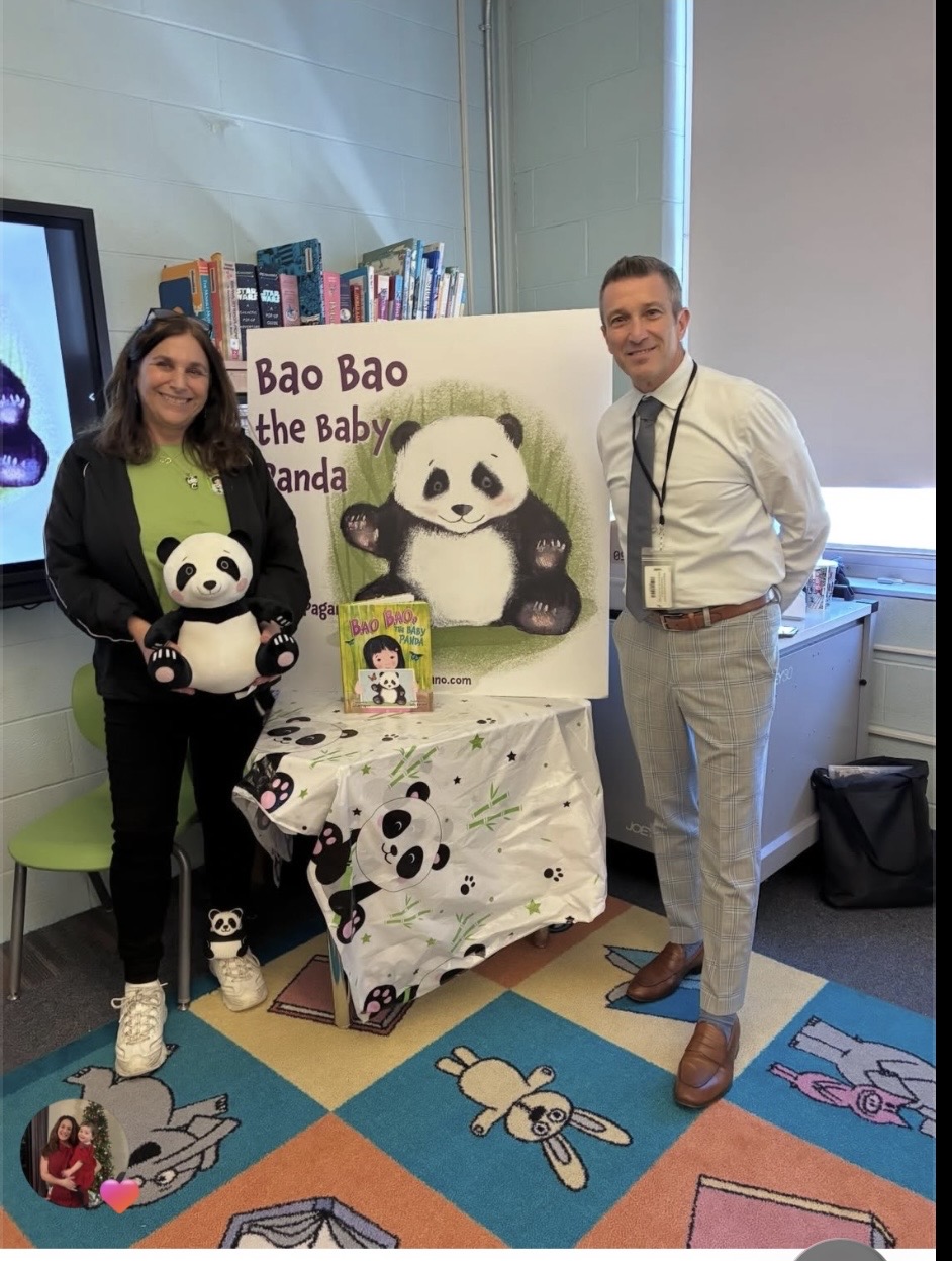 Two people standing next to a display with a panda illustration, holding a panda plush toy, in a room with colorful floor tiles.