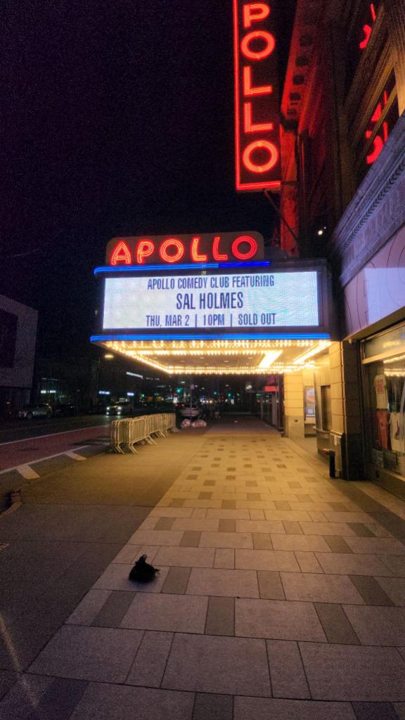 Night view of Apollo theater marquee with illuminated signs and sidewalk, no people visible.