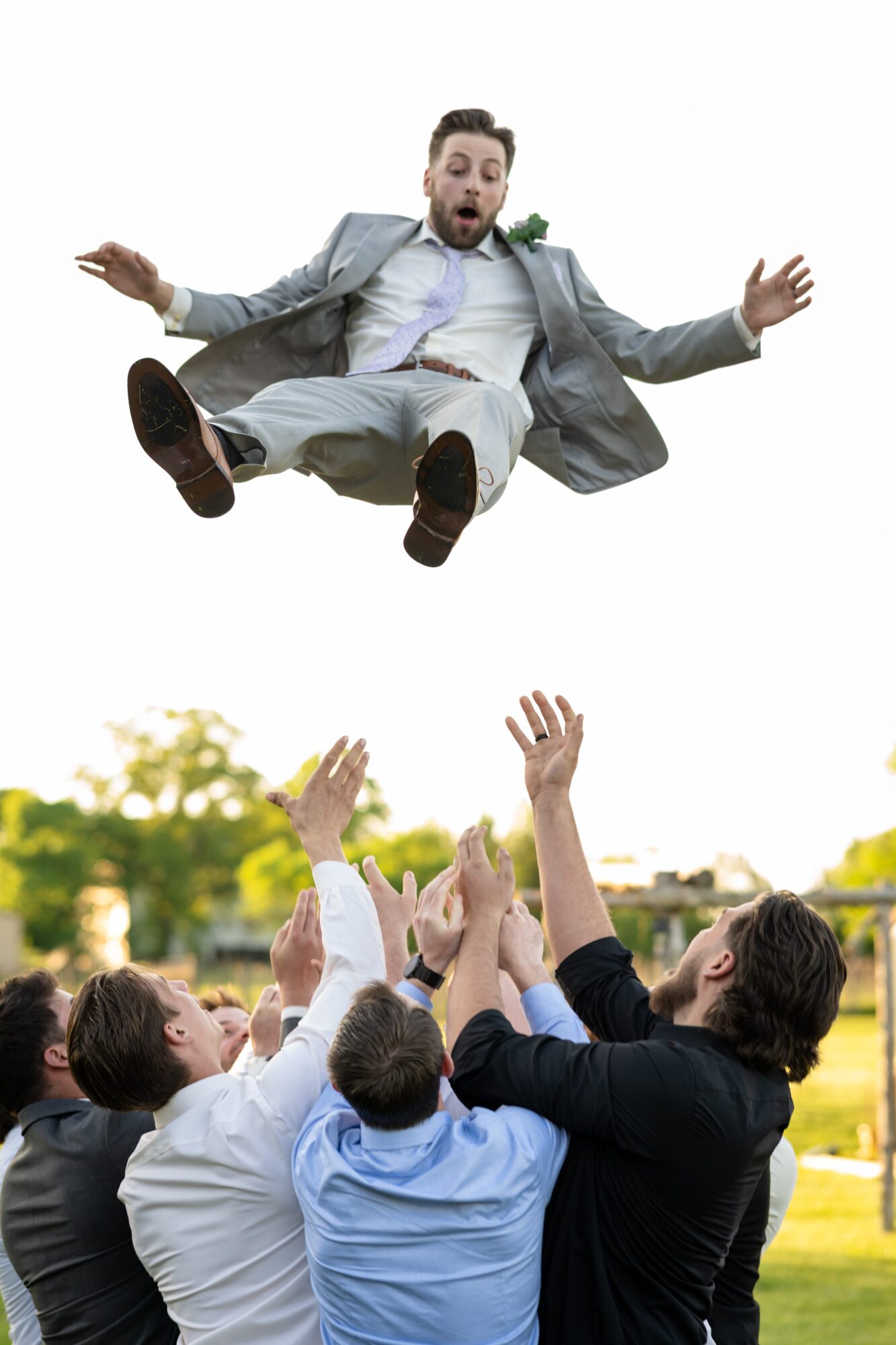 Man in suit falling from sky onto group of people raising hands outdoors, trees and sky in background.
