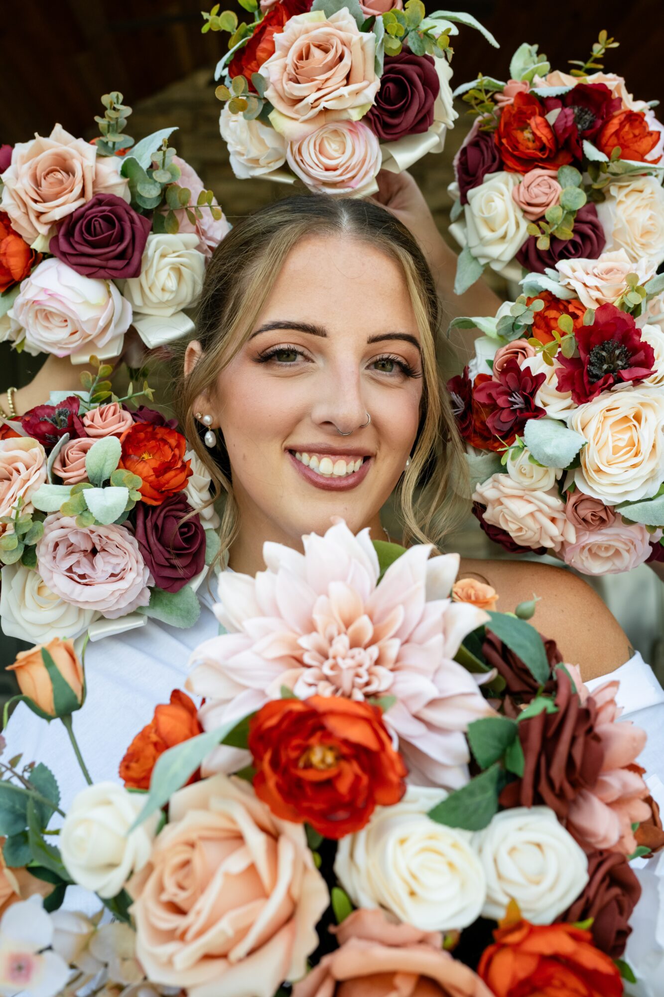 Smiling woman surrounded by colorful flowers, holding a large bouquet in front of her face.