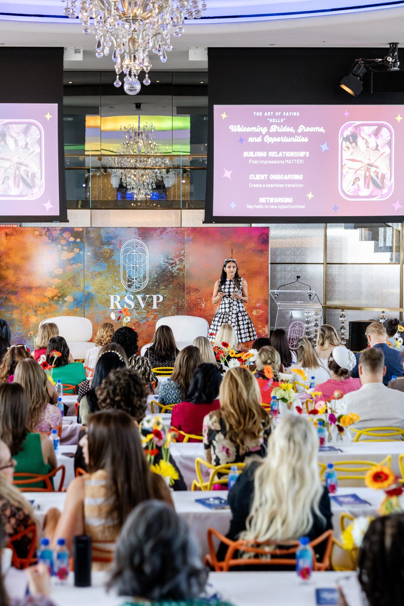 Large event space with a stage, screens, and a chandelier, filled with children and adults seated at decorated tables.